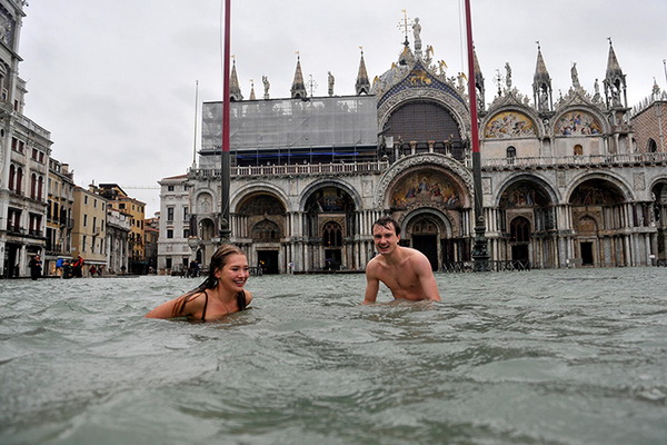 A young man and a woman swim in flooded St Mark's Square,Venice
